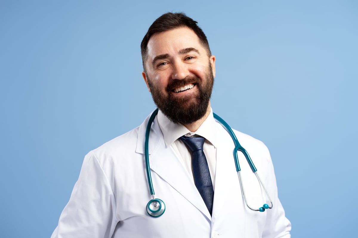 Studio portrait of a smiling doctor wearing a stethoscope looking at camera on a blue background