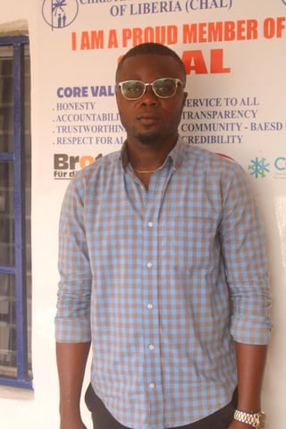 Man wearing glasses and blue checkered shirt standing in front of organizational banner with core values listed