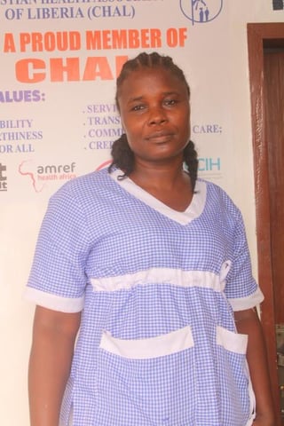 Woman wearing a purple gingham dress standing in front of an organizational banner with logos and text about healthcare values