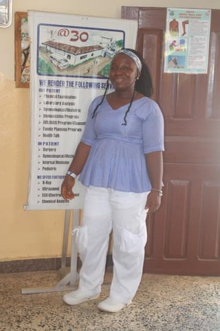Woman in blue checkered shirt and white pants stands in front of medical clinic information posters